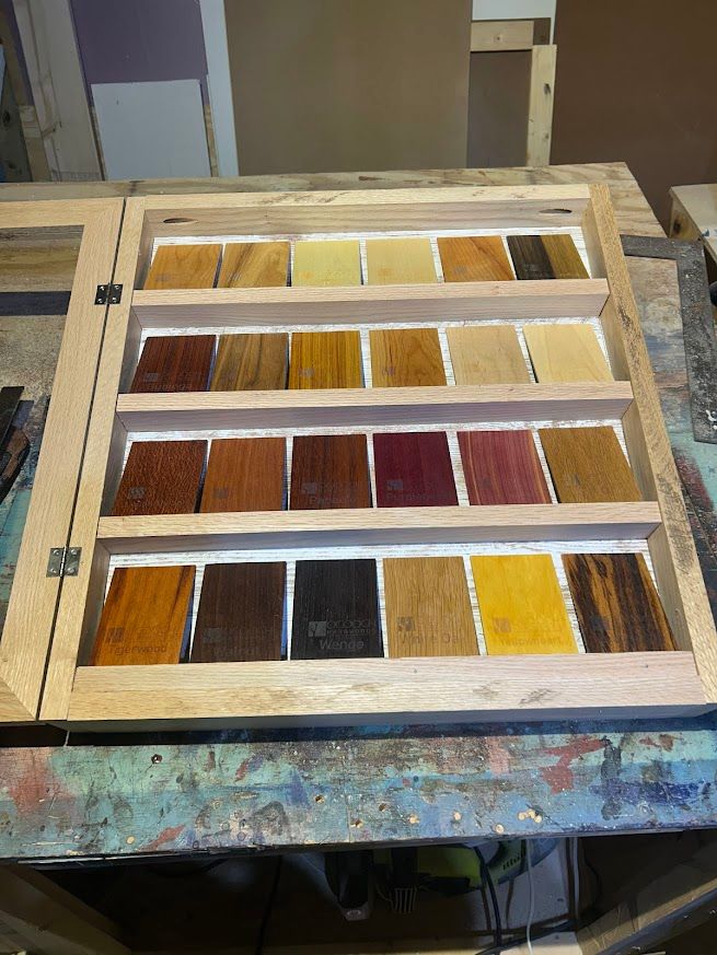 A wooden cabinet displaying a variety of stained wood color samples in rows.