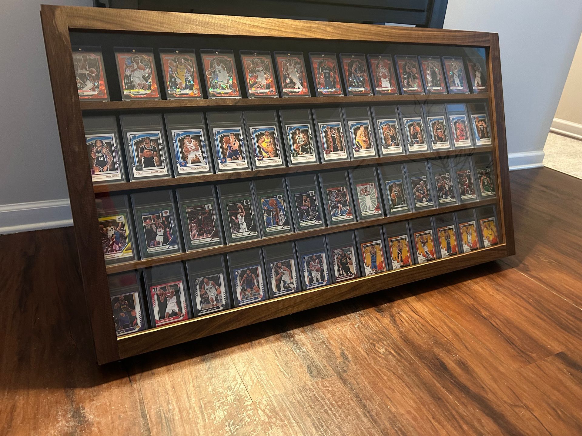 Wooden display case holding many trading cards, sitting on a wooden floor. The cards are visible through glass.
