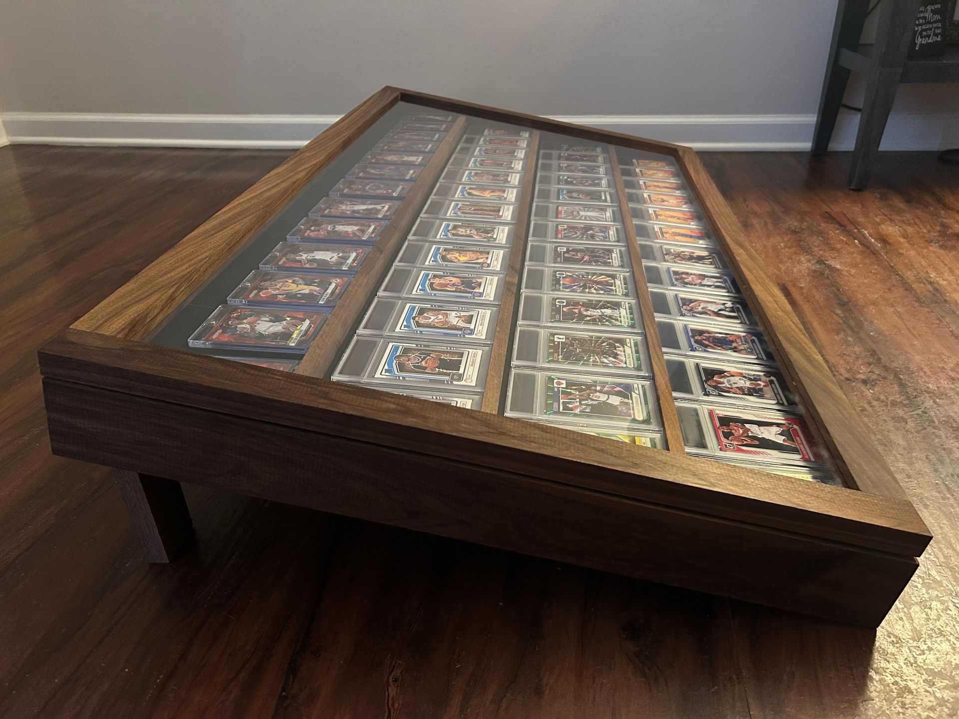 Wooden display case with tilted glass top, filled with rows of trading cards on a hardwood floor.