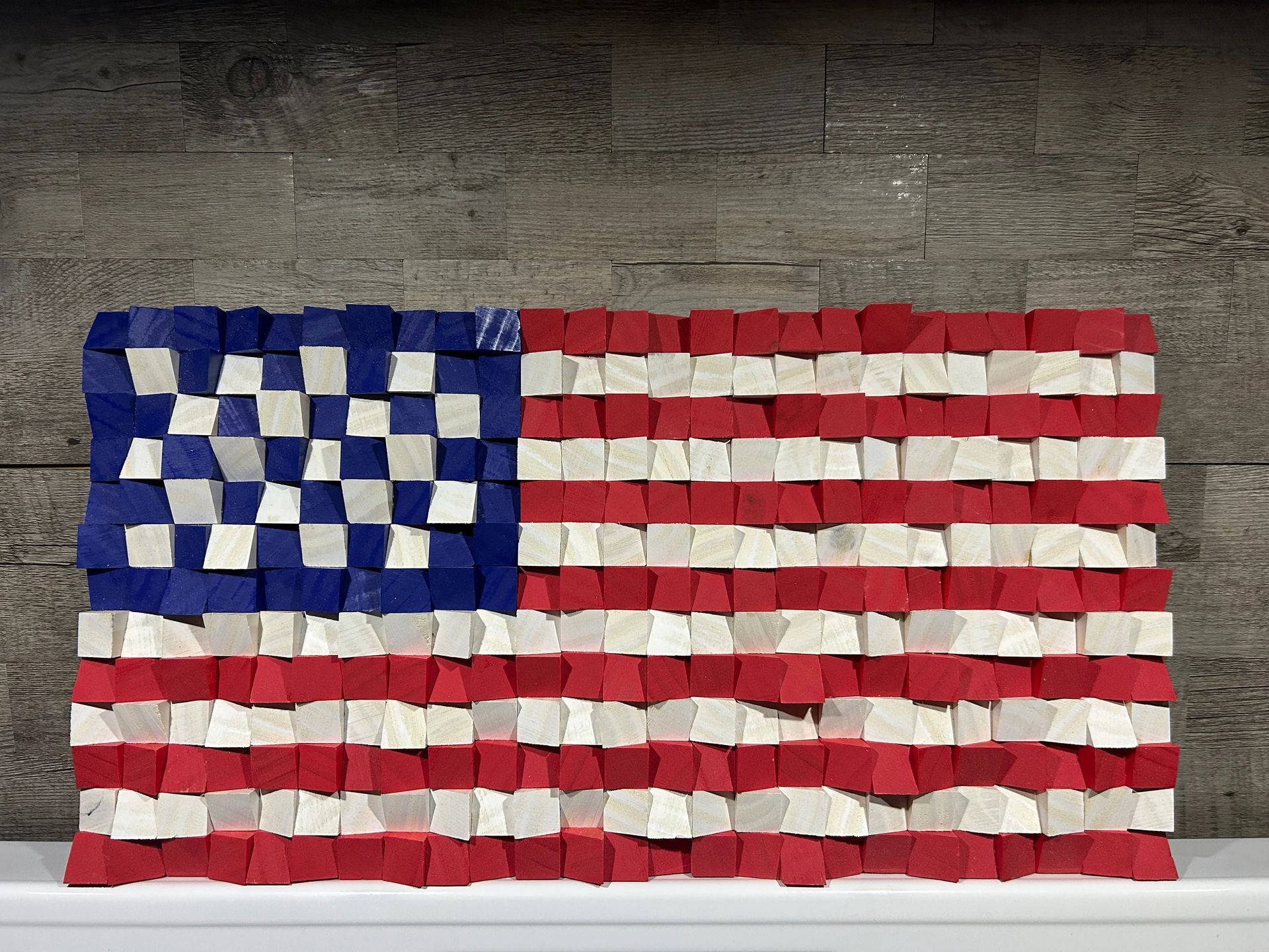 Wooden American flag made of red, white, and blue blocks against a neutral wall.