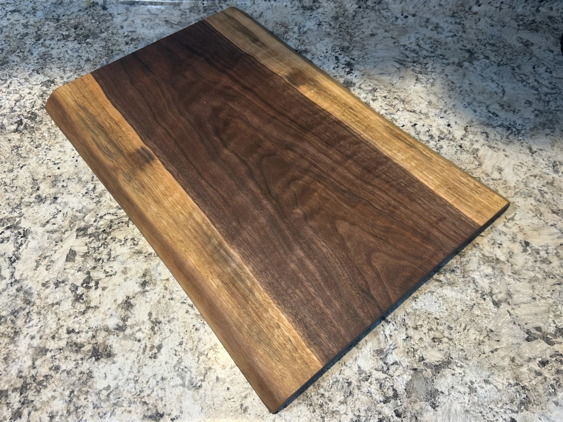 Wooden cutting board on a countertop with a dark wood center and lighter borders.