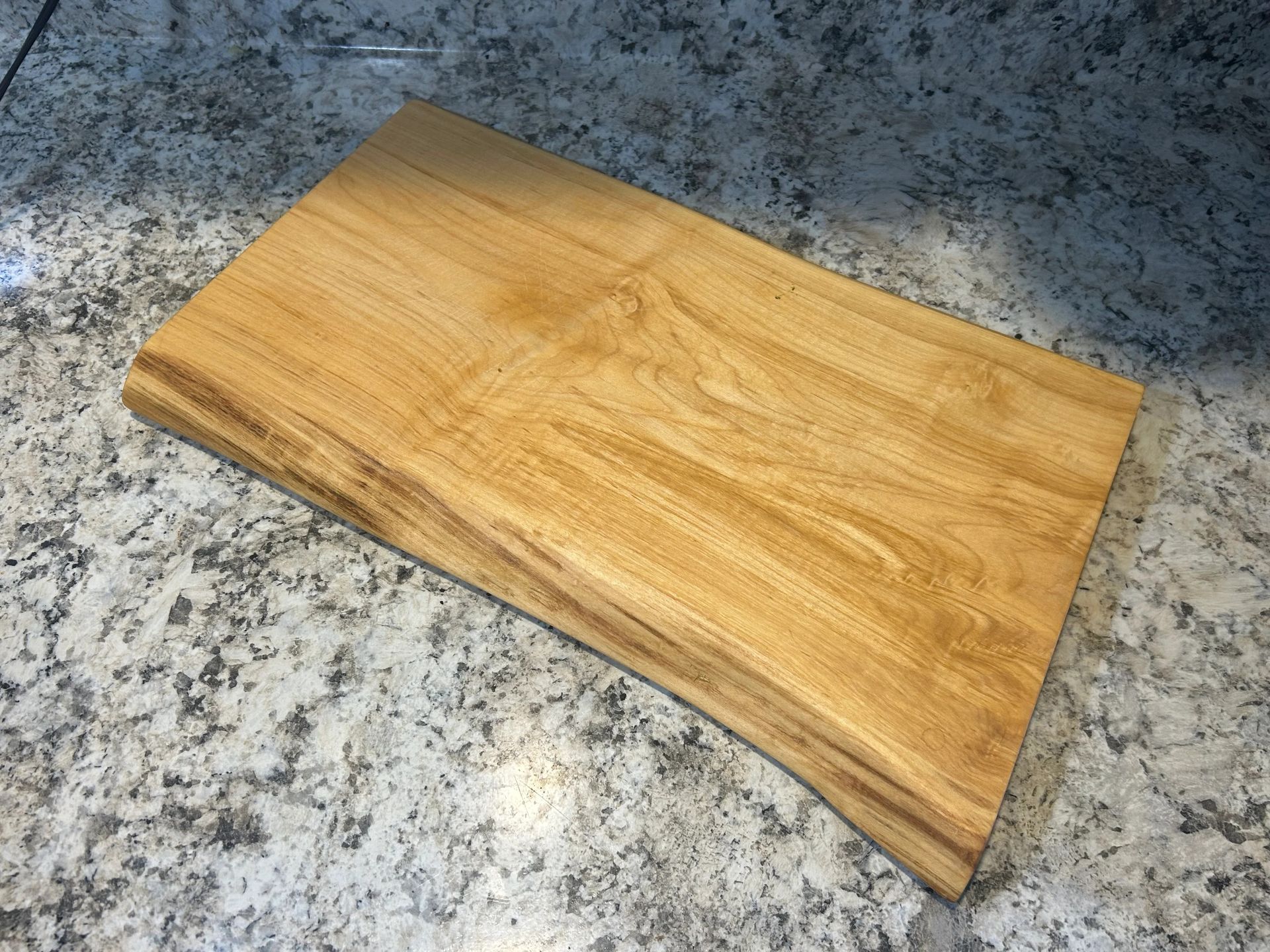 Wooden cutting board with a live edge on a granite countertop.