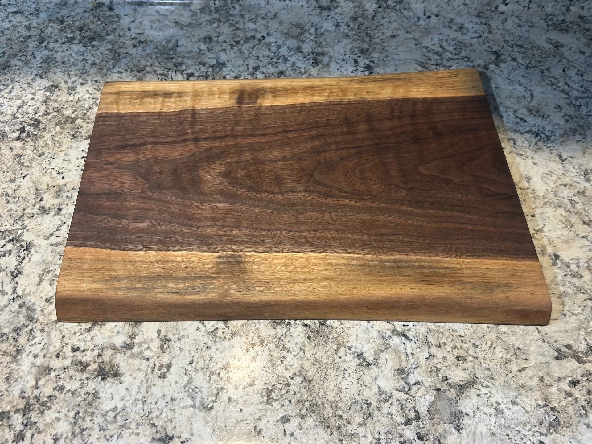 Wooden cutting board on a countertop with a dark wood center and lighter borders.