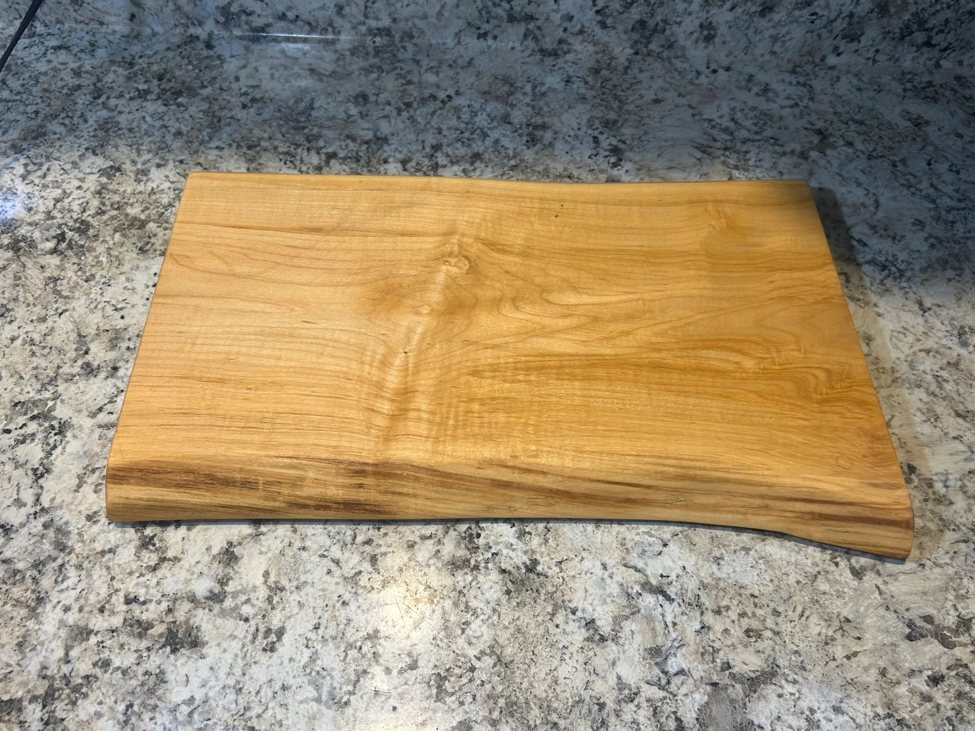 Wooden cutting board with a live edge on a granite countertop.