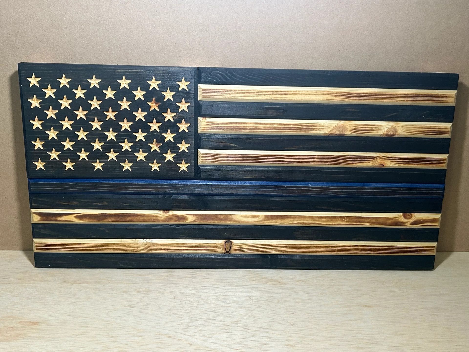 Wooden American flag with black stars, blue line, and burnt wood stripes.