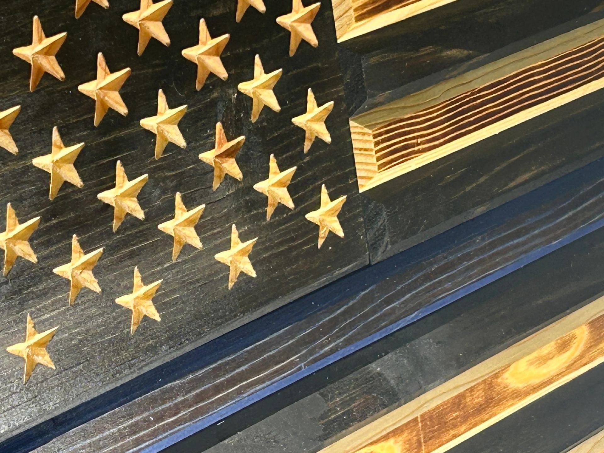 Wooden American flag with black stars, blue line, and burnt wood stripes.