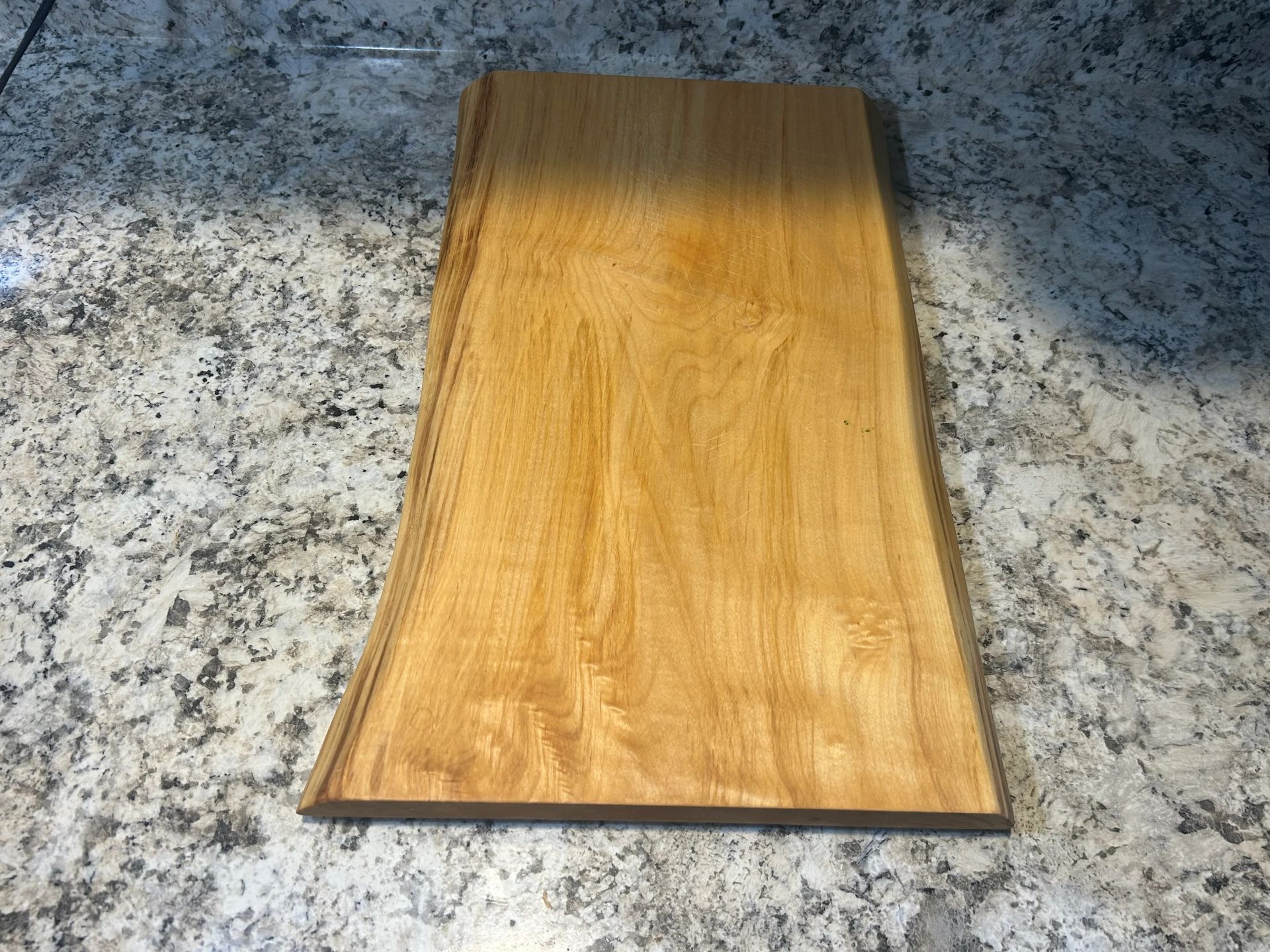 Wooden cutting board on a speckled countertop. The board has a live edge.