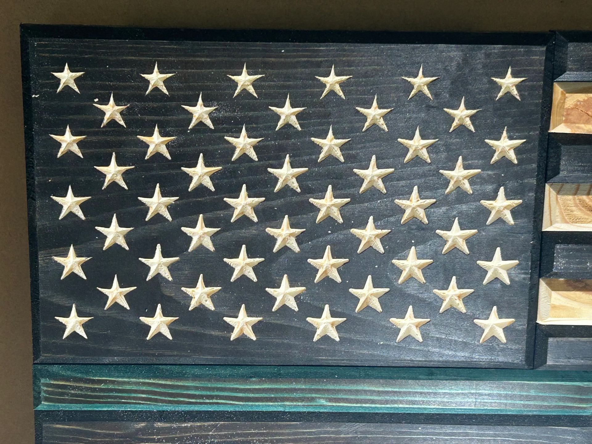 Carved wooden American flag with black background, white stars, and blue line.
