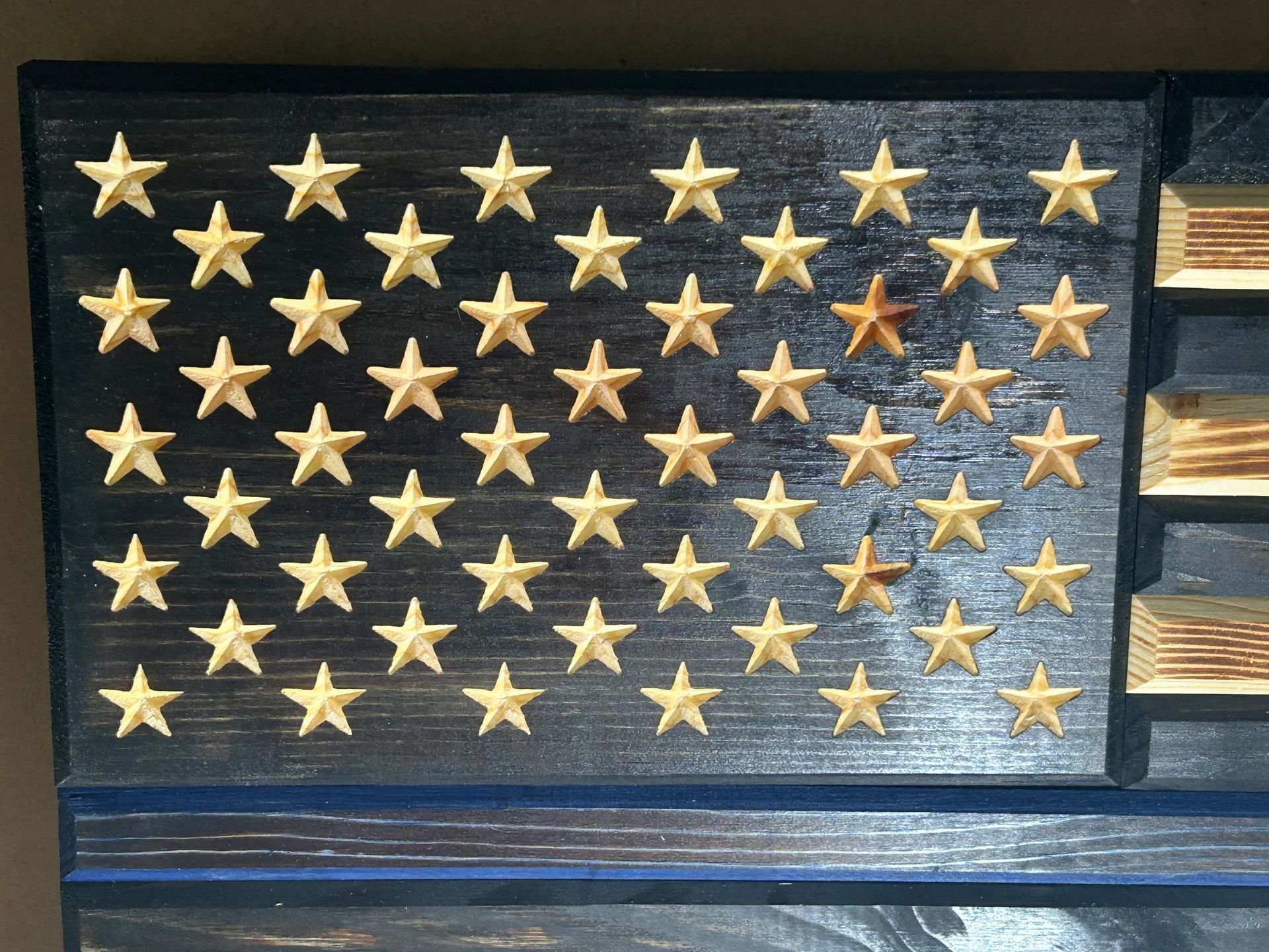 Wooden American flag with carved stars on a dark, stained background.