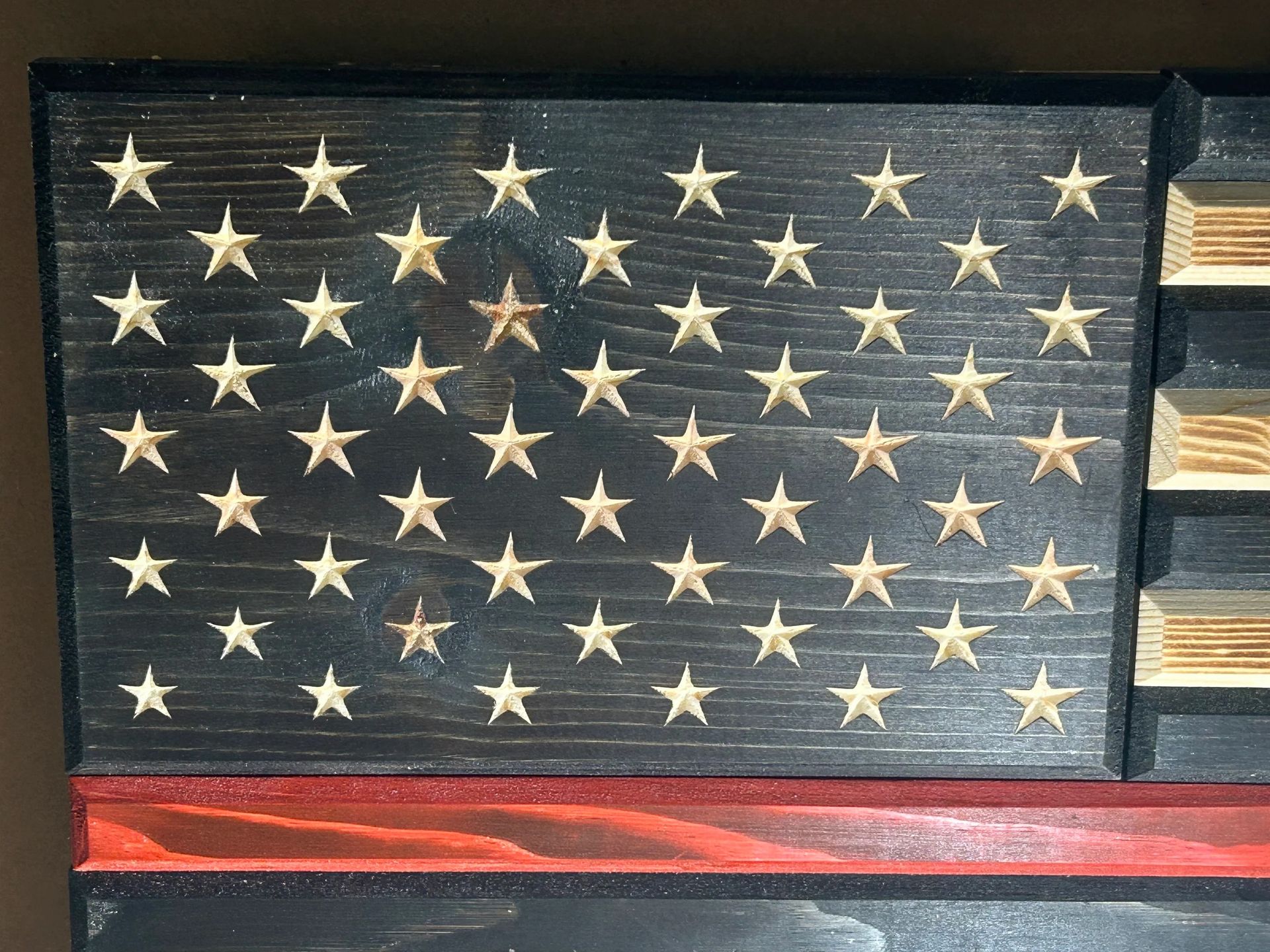 Wooden American flag art with carved stars, black field, red stripe.