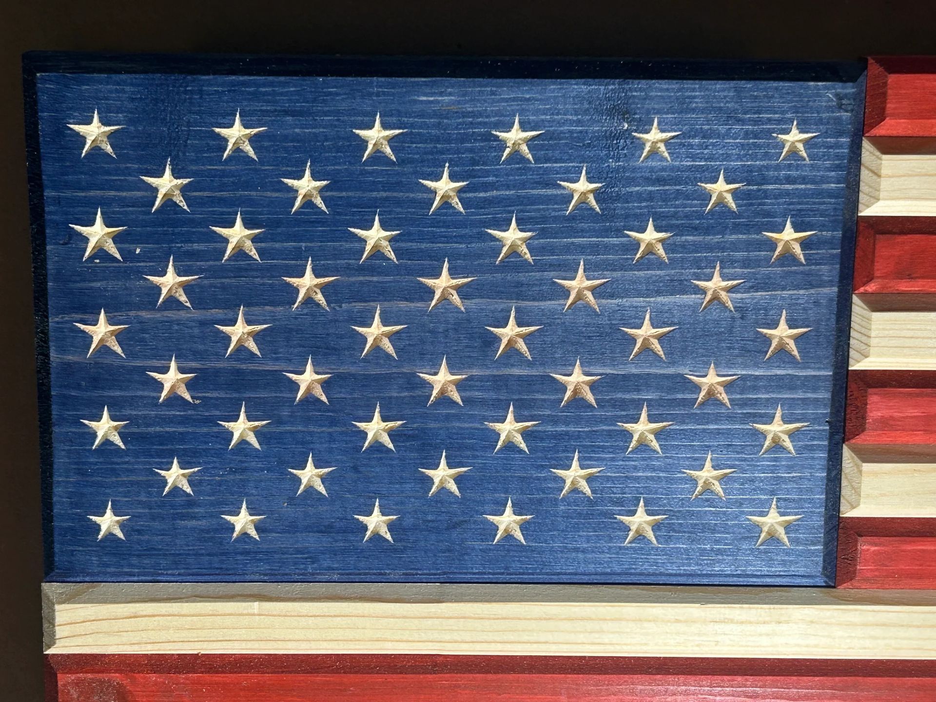 Wooden American flag carving with blue star field and red and white stripes.