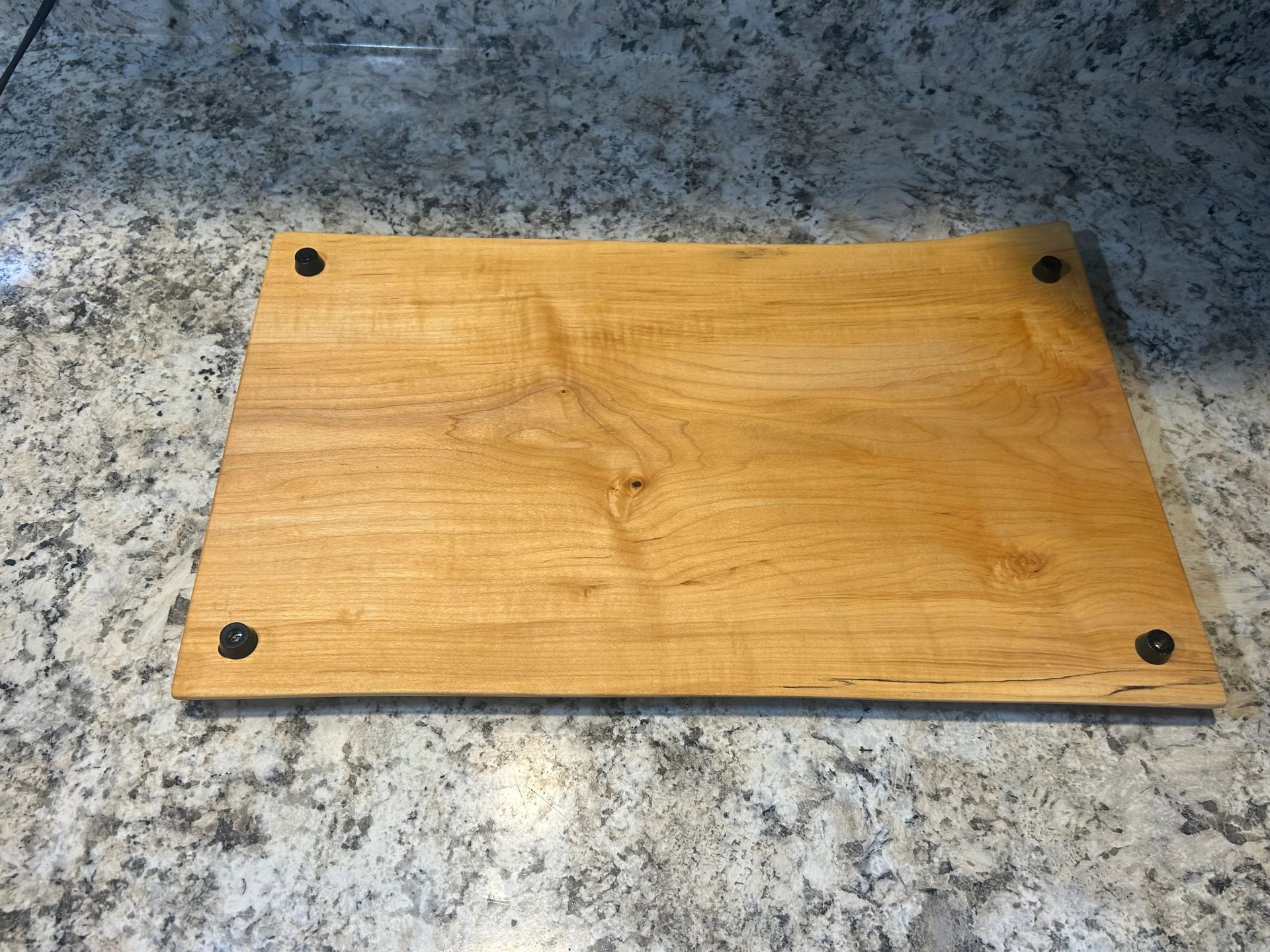 Wooden cutting board with dark feet, on a granite countertop.