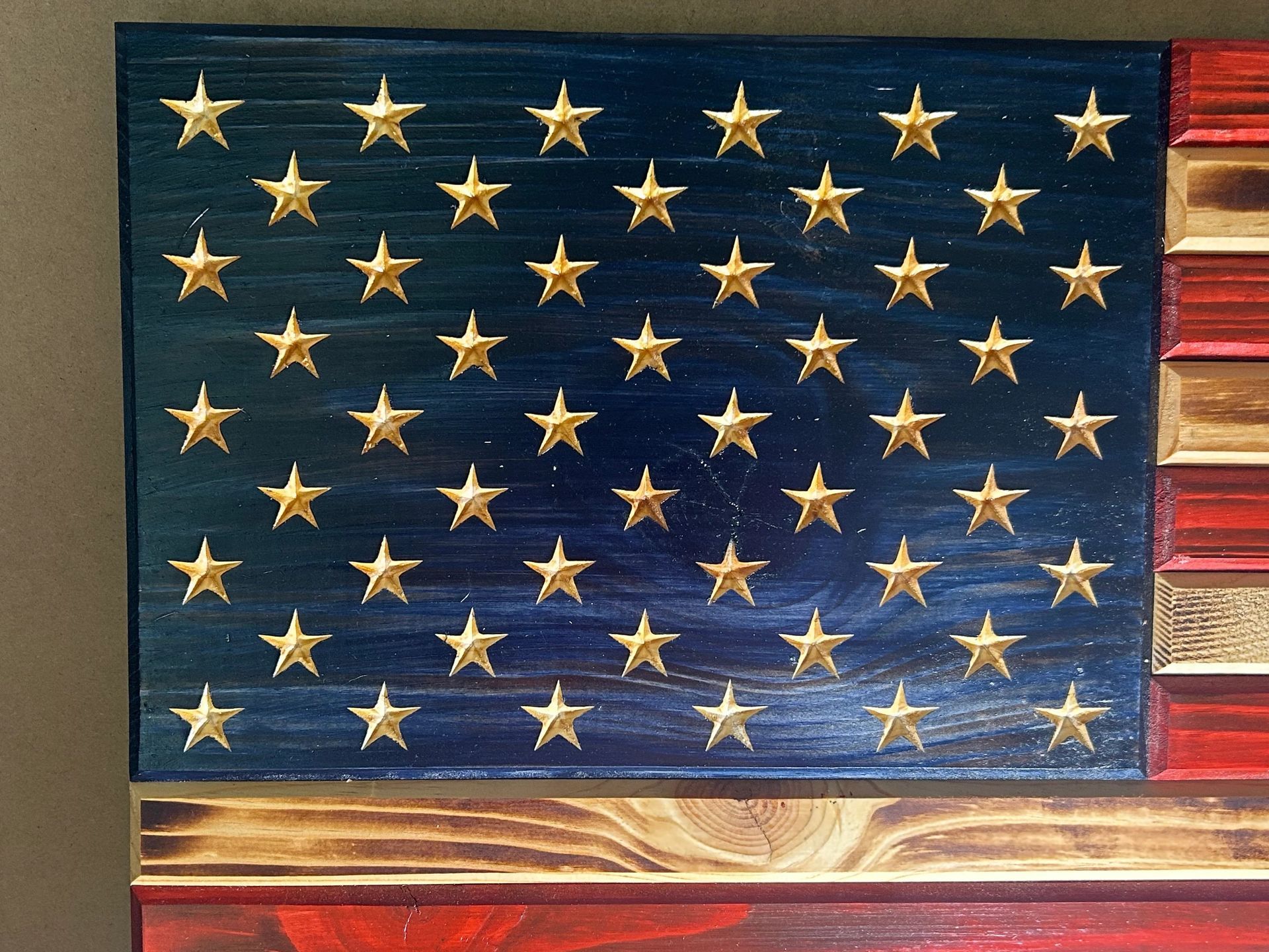 Wooden American flag with golden stars, blue field, red and white stripes.