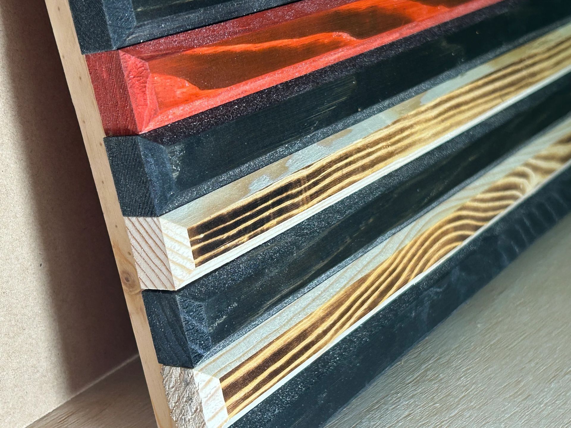 Close-up of a wooden American flag, with burnt wood stripes and red stripes; the other stripes are painted black.
