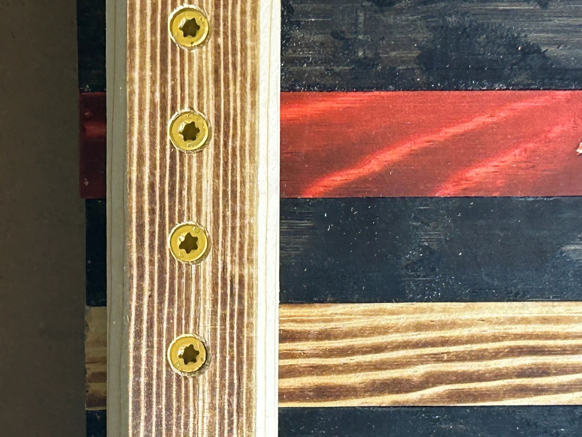 Close-up of wooden flag with black, red, and tan stripes, secured with gold screws.