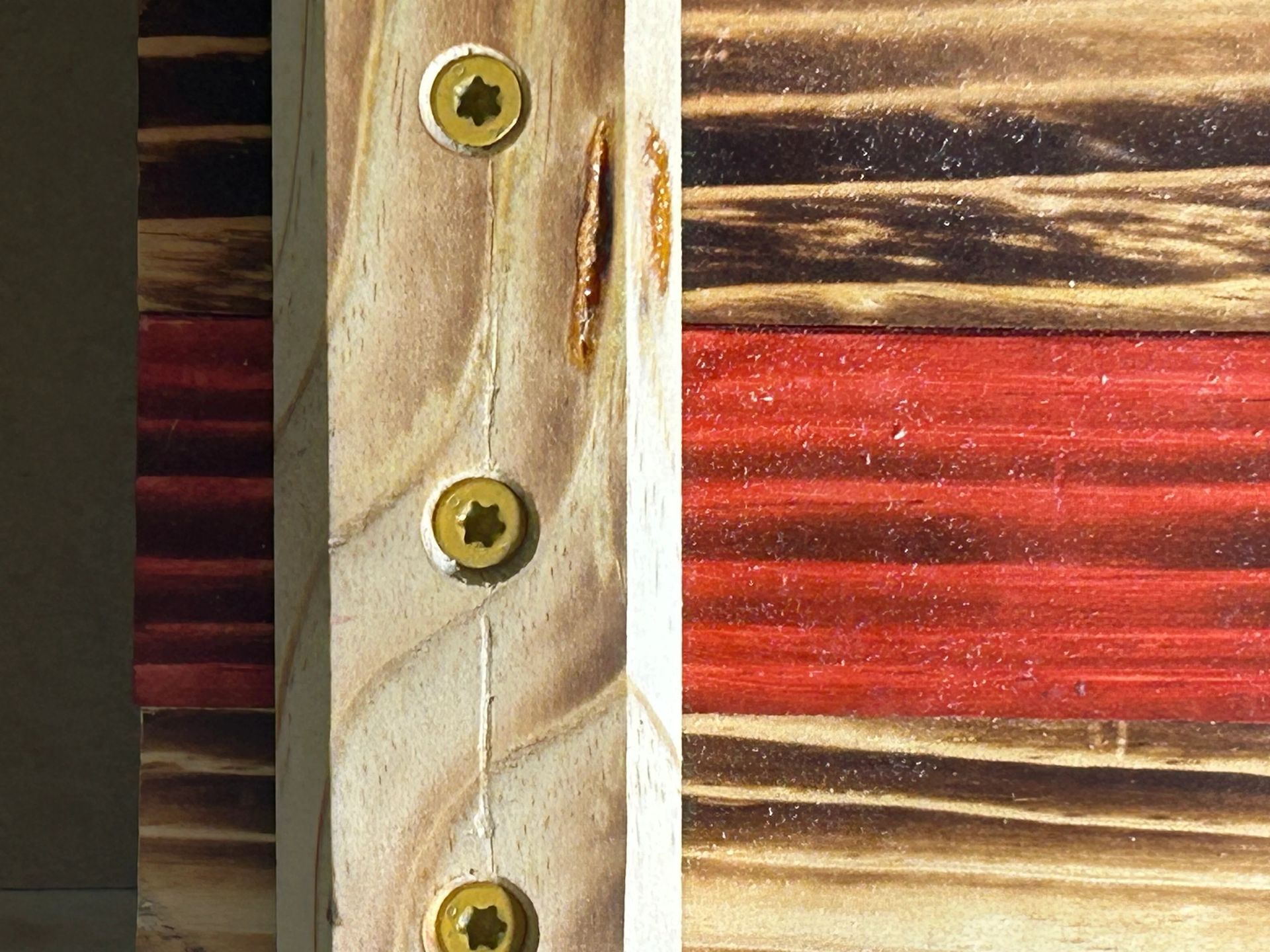 Close-up of a wooden American flag, showing red and charred wooden stripes, with a central wooden support post.