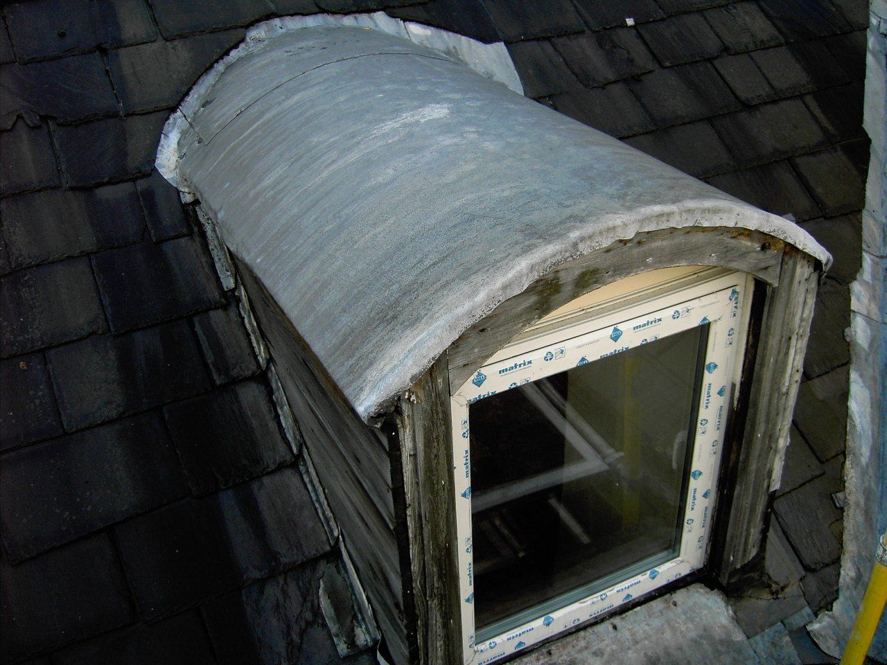 Dormer window with curved, light-colored roof on a shingled roof.