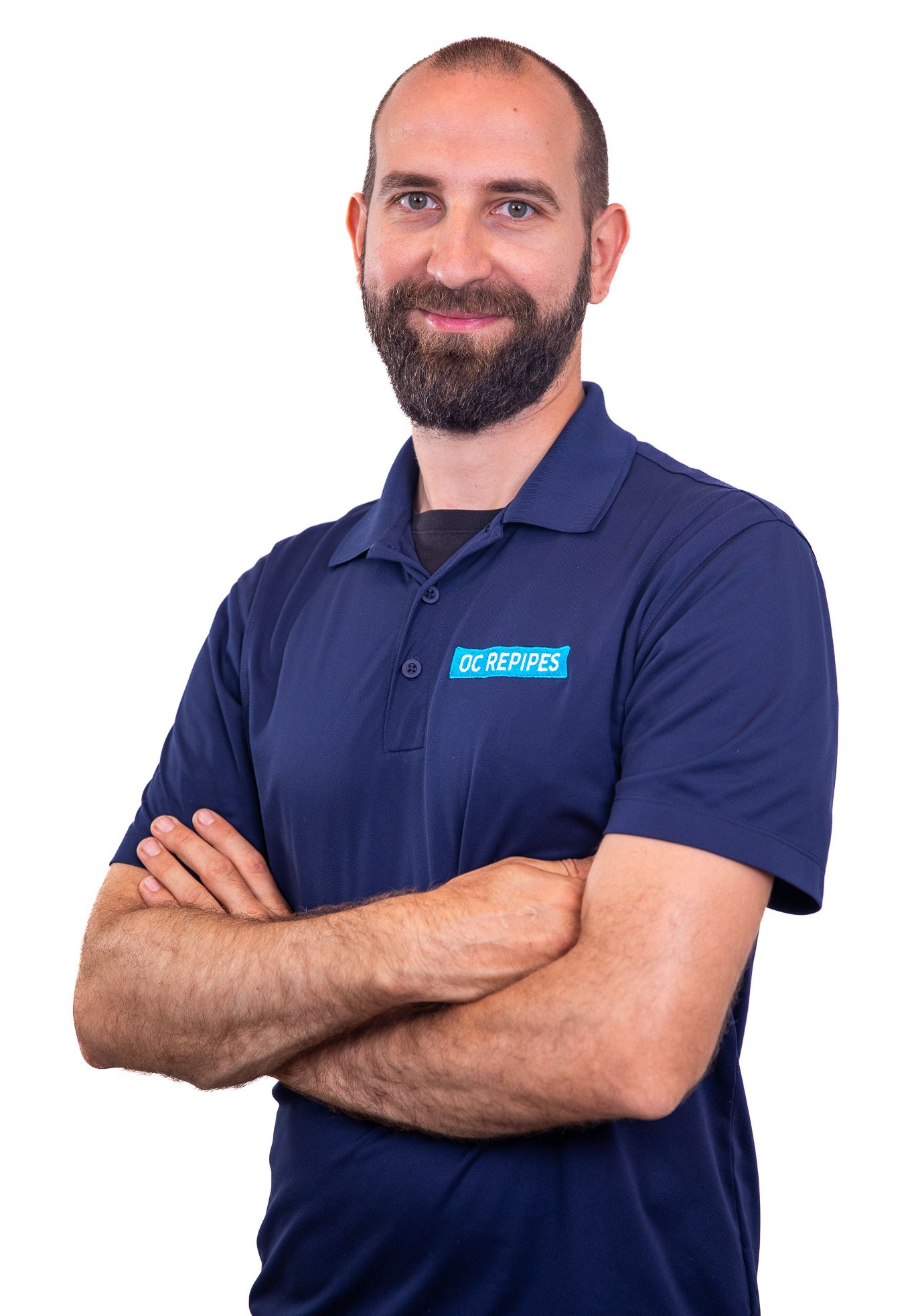Man with a beard wearing a blue polo shirt with arms crossed, smiling.