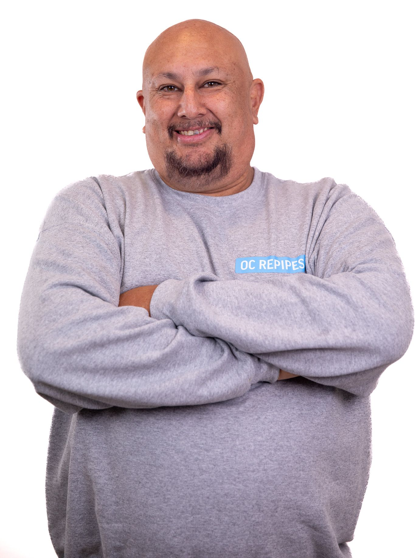 Bald man in gray sweatshirt with arms crossed, smiling.