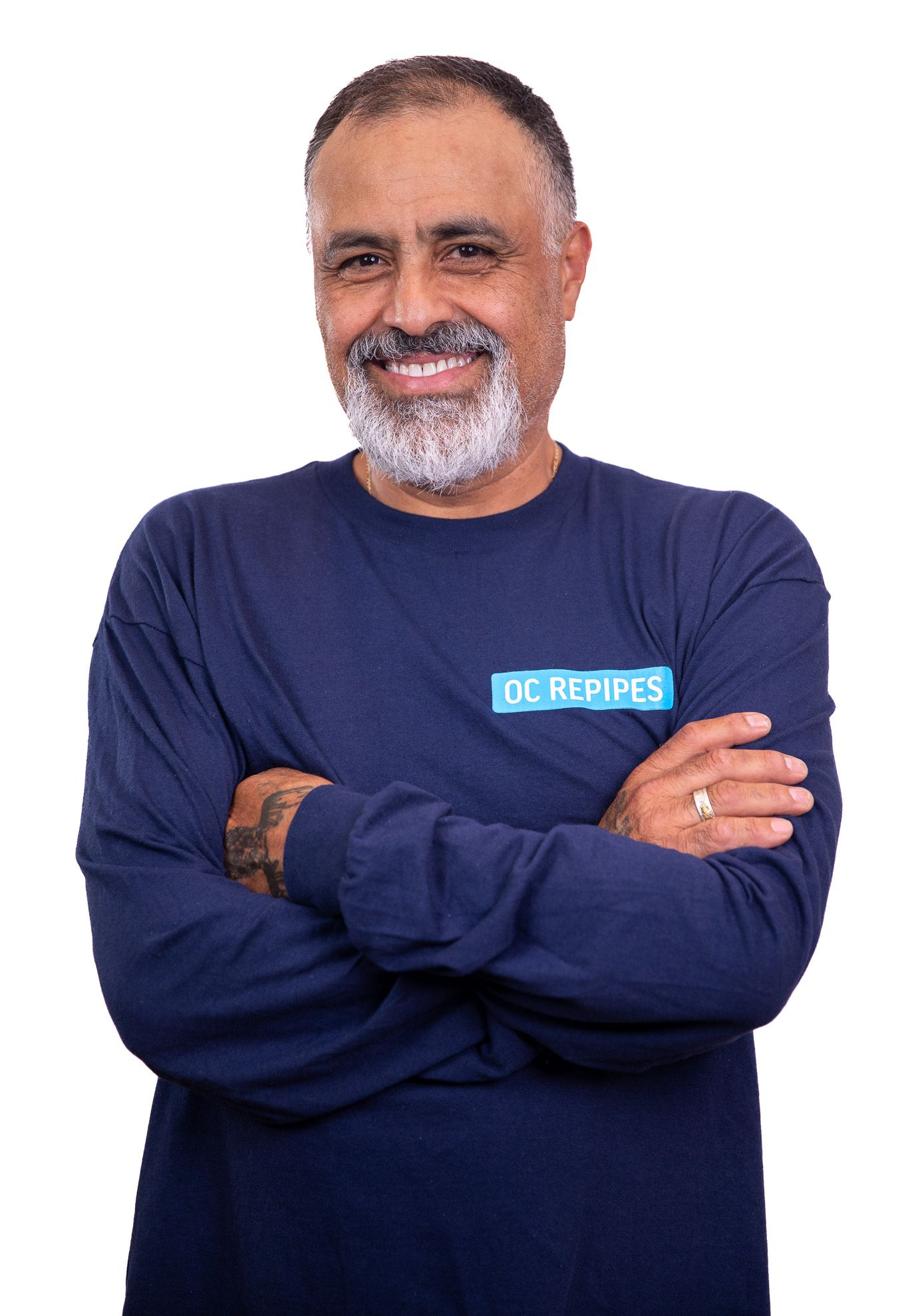 Man with arms crossed, smiling; wearing a blue long-sleeved shirt that says 