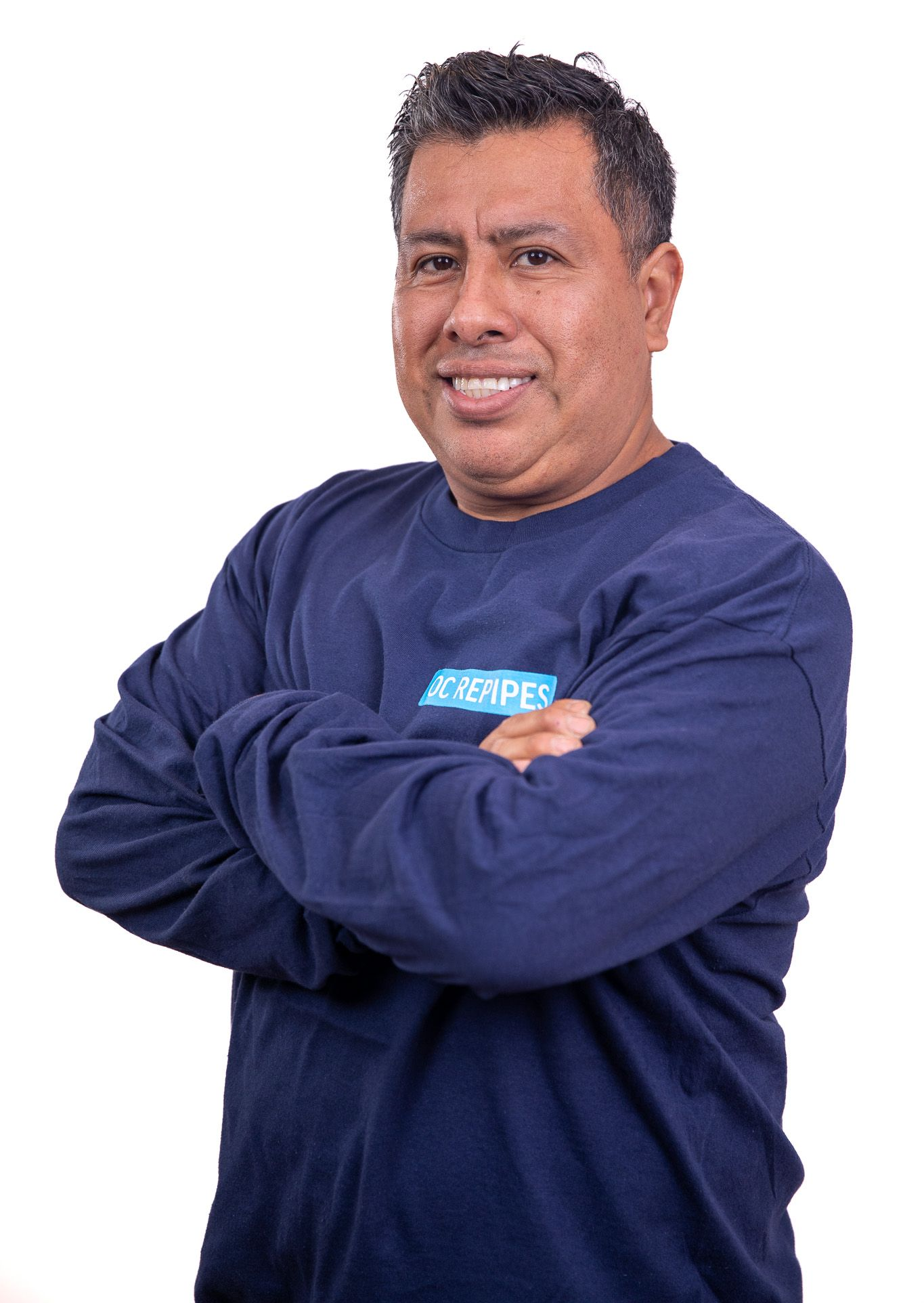 Man with crossed arms, smiling, wearing a navy blue long-sleeved shirt, white background.