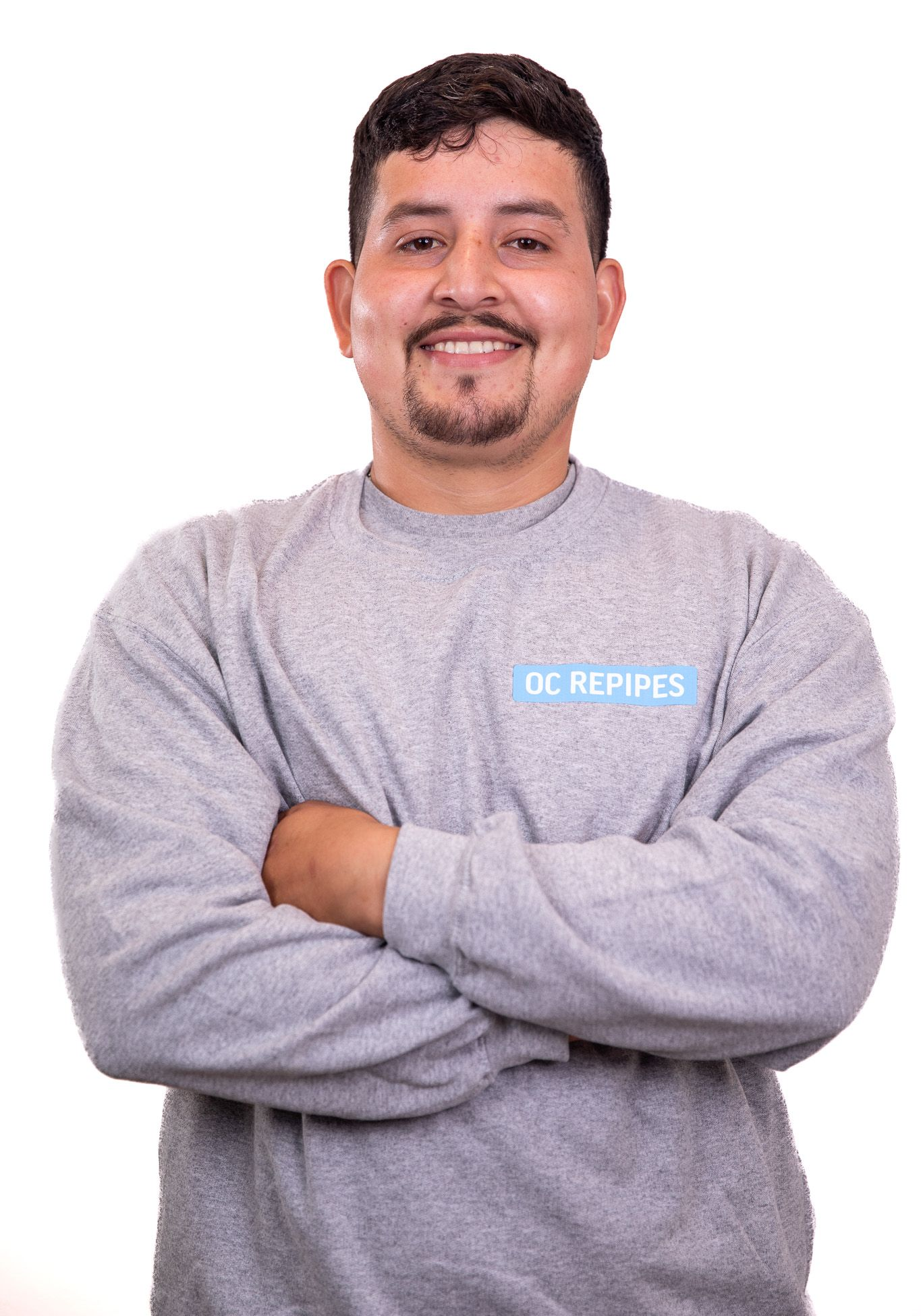 Man with arms crossed, smiling, wearing a grey sweatshirt with 