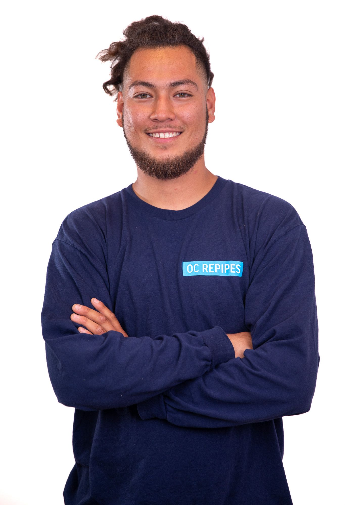 Man with arms crossed smiling, wearing a blue long-sleeve shirt with a logo for OC Repipes.