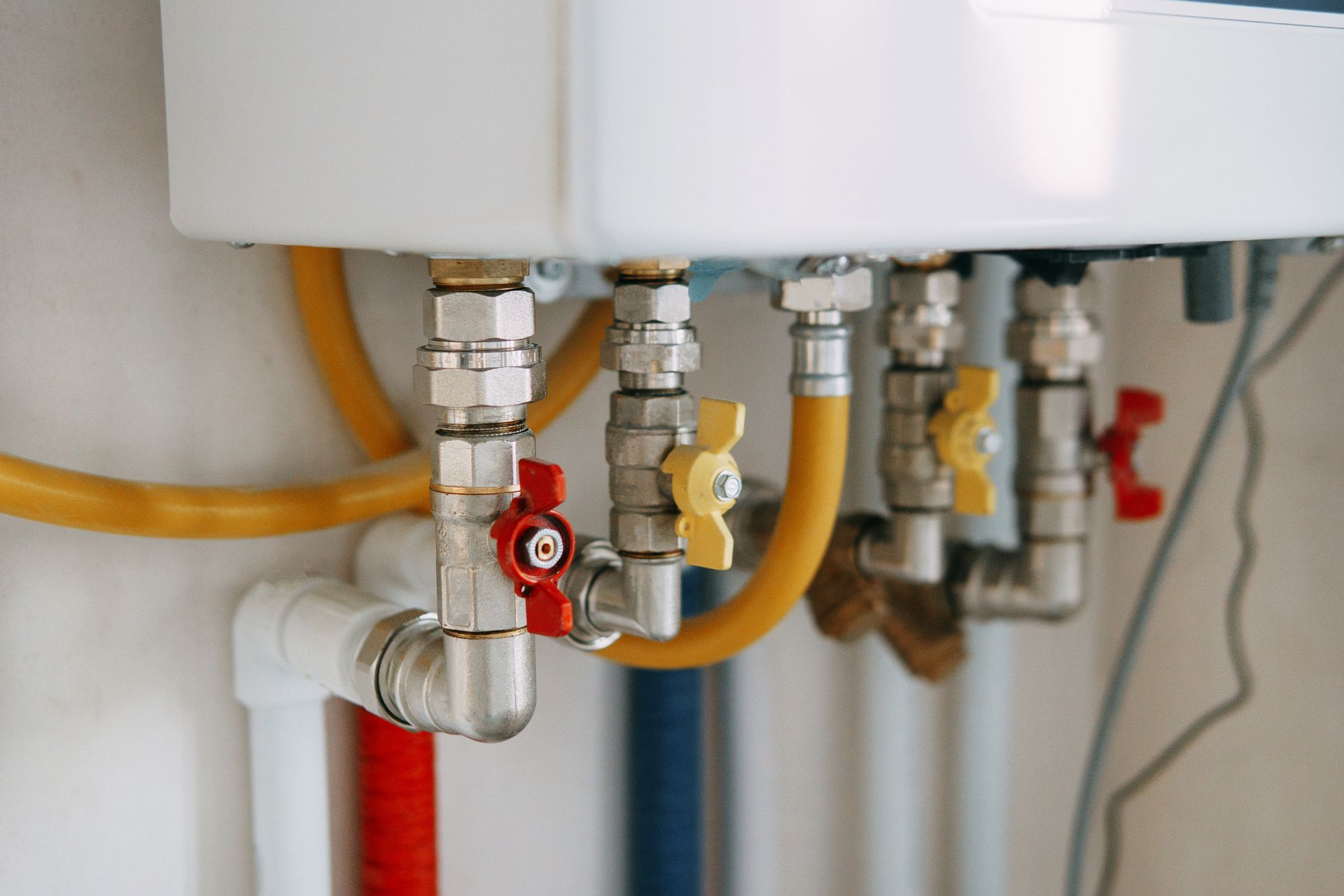 Close-up of a white appliance with multiple pipes, valves, and gas lines, including red, yellow, and silver components.