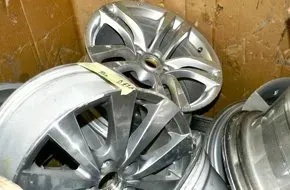 A stack of several silver, multi-spoke automotive alloy wheels sitting inside a cardboard container.