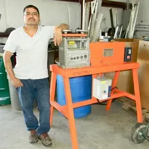 A person standing next to an orange wire stripping machine in a workshop.