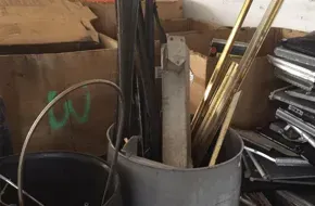 A container holds long metal pipes, rods, and scrap materials in a warehouse storage area.