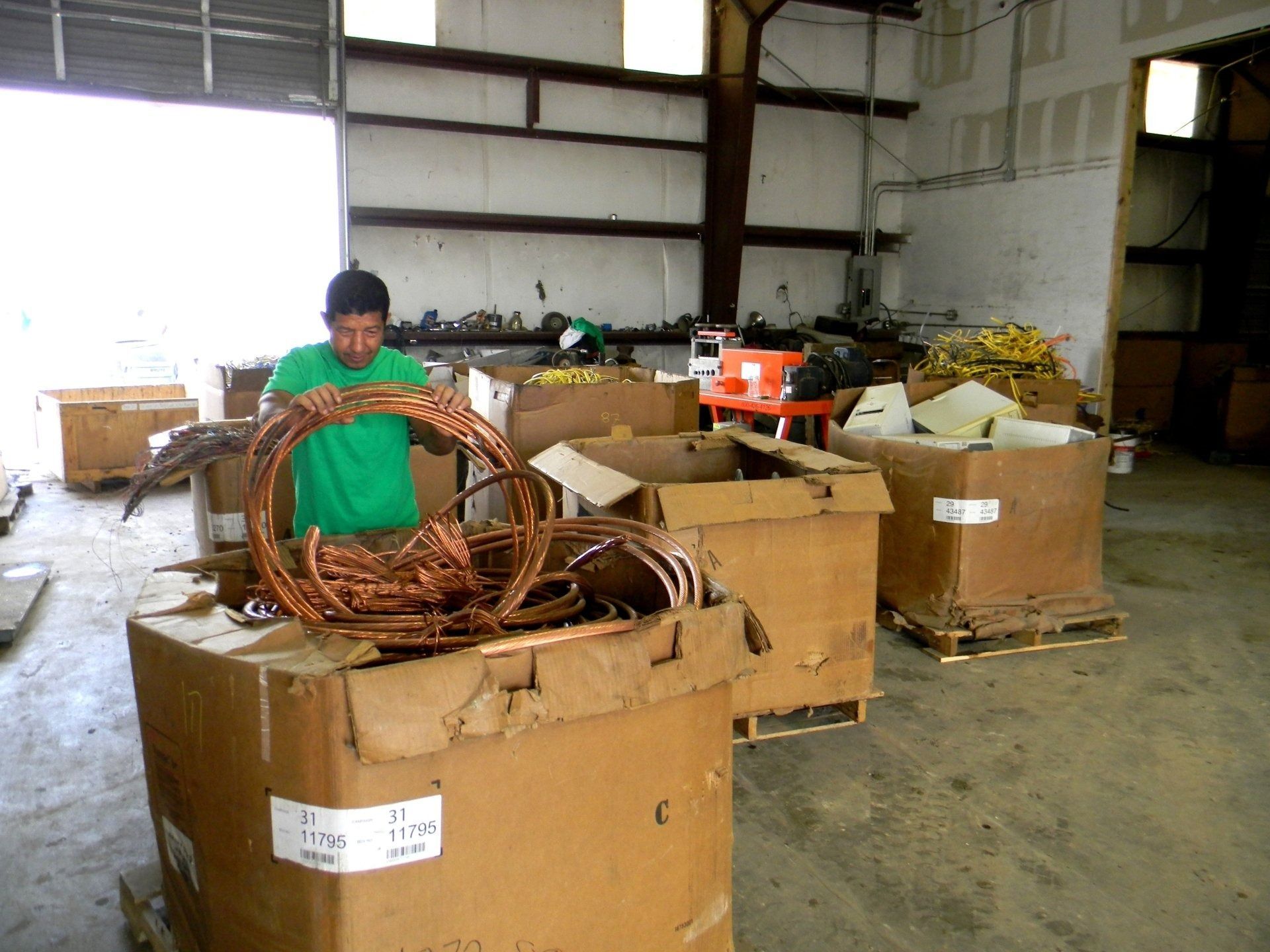 A person in a green shirt sorting coiled copper wire into large cardboard boxes inside a warehouse.