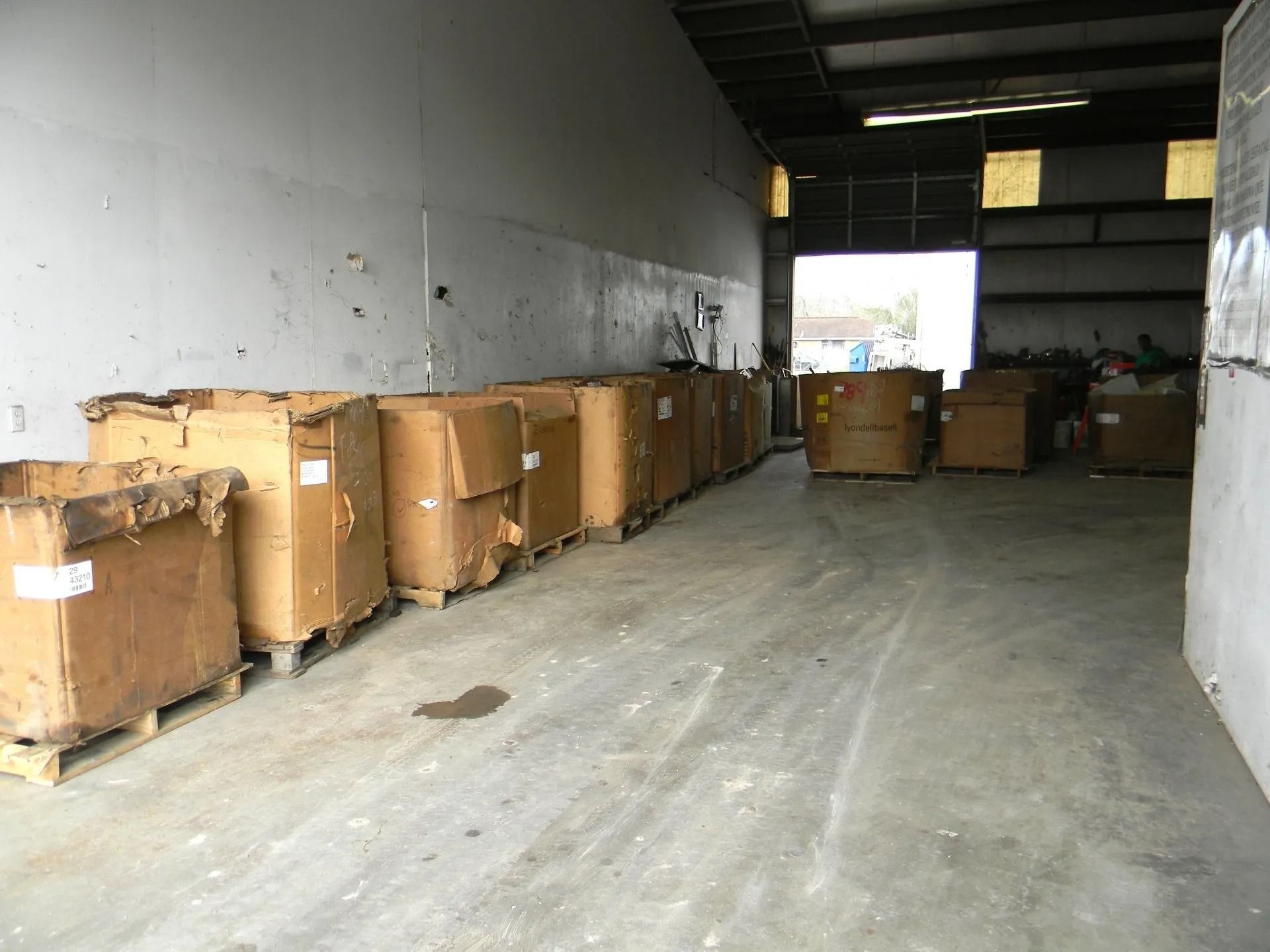 A row of large, tan cardboard shipping bins sitting on wooden pallets inside an empty warehouse.