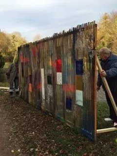 Debbie Nuttall Artist | a man is standing next to a wooden fence with a painting on it .