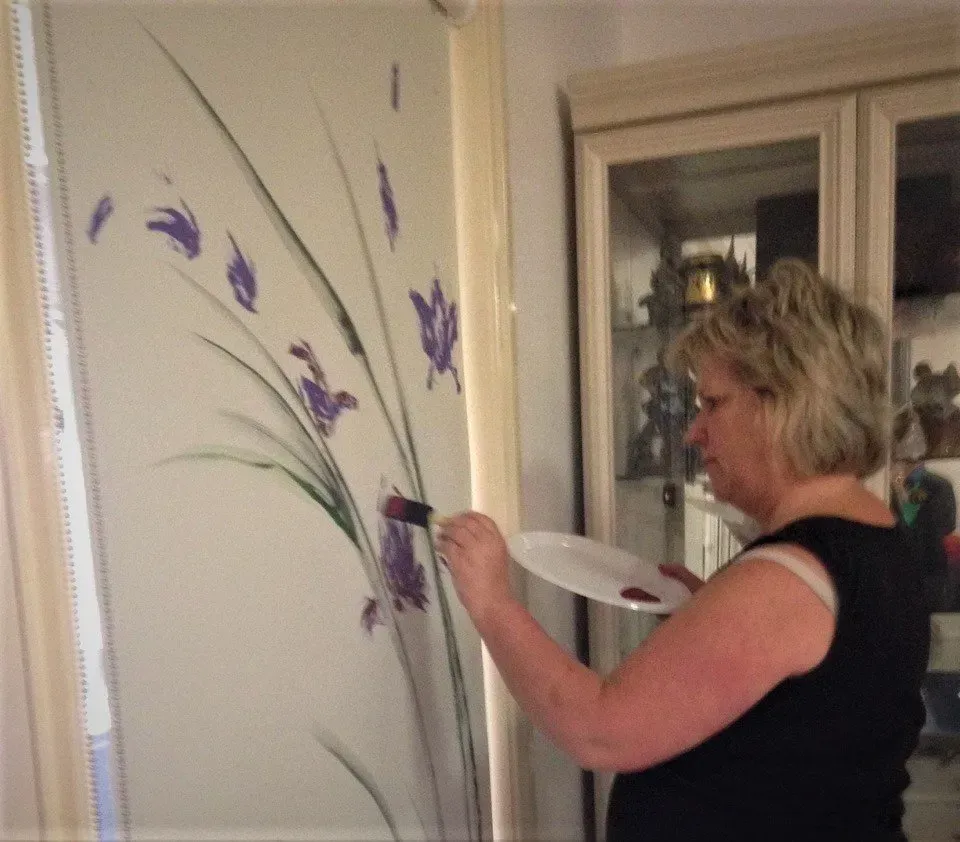 Debbie Nuttall Artist | a woman paints flowers on a wall with a brush