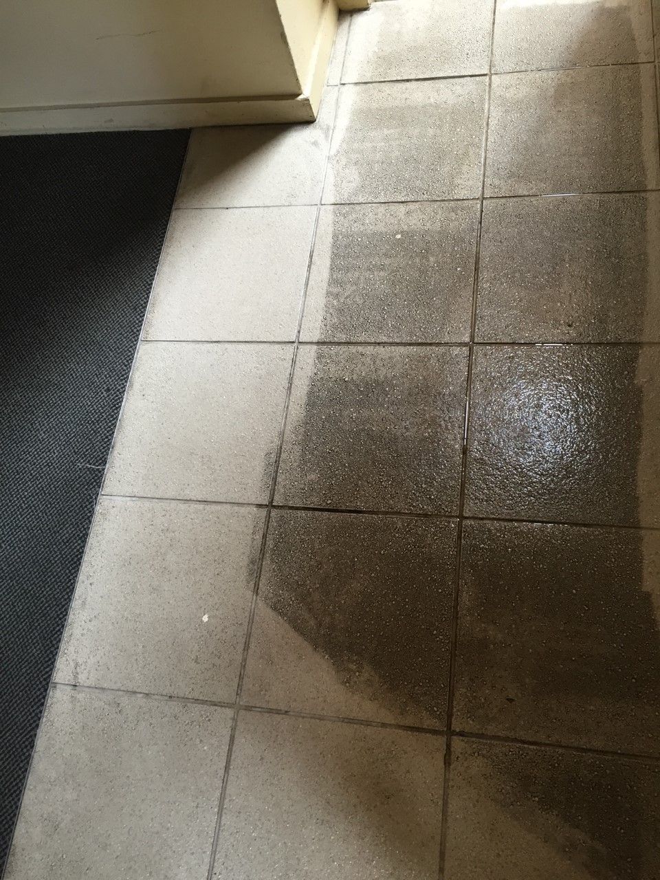 Dirty, light-colored tile floor in front of a door and dark floor mat. Visible dirt is present — Enviro Clean Carpet and Tile Cleaning in Budgewoi, NSW