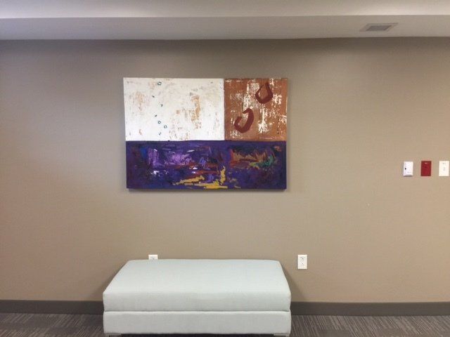 A painting hangs on a wall above a white ottoman