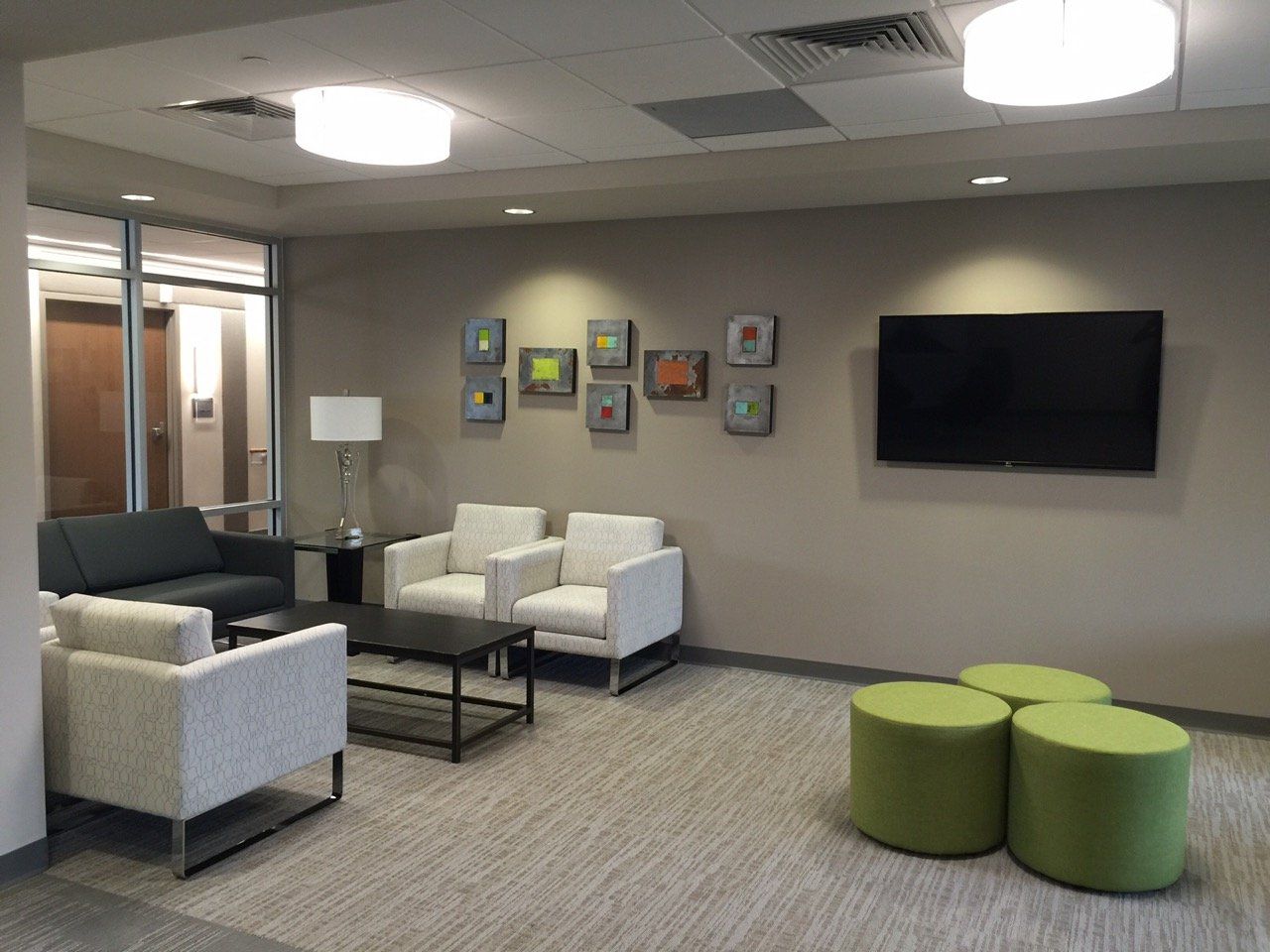 A living room with a couch , chairs , ottomans and a flat screen tv.