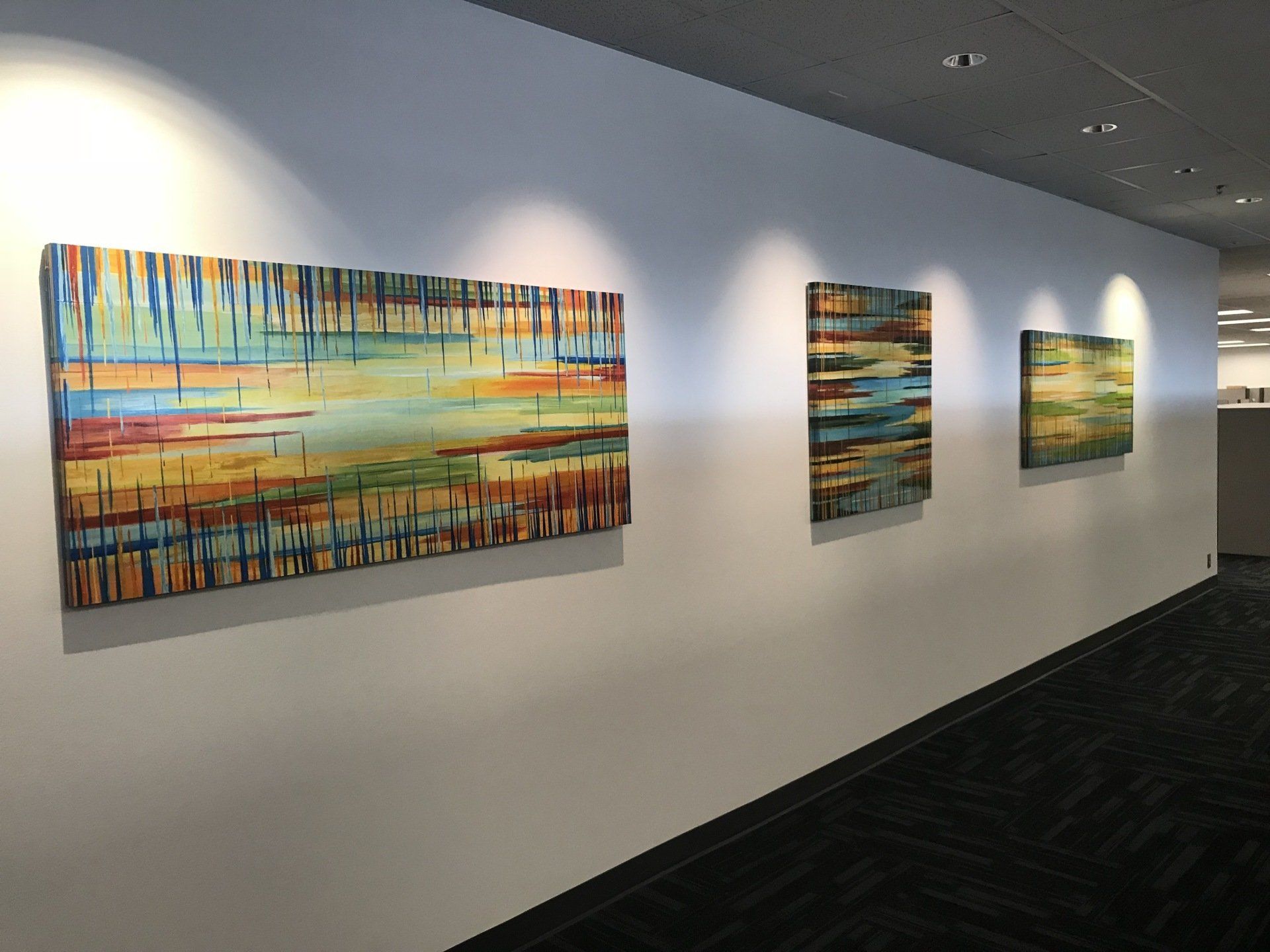 Three paintings are hanging on a wall in a hallway