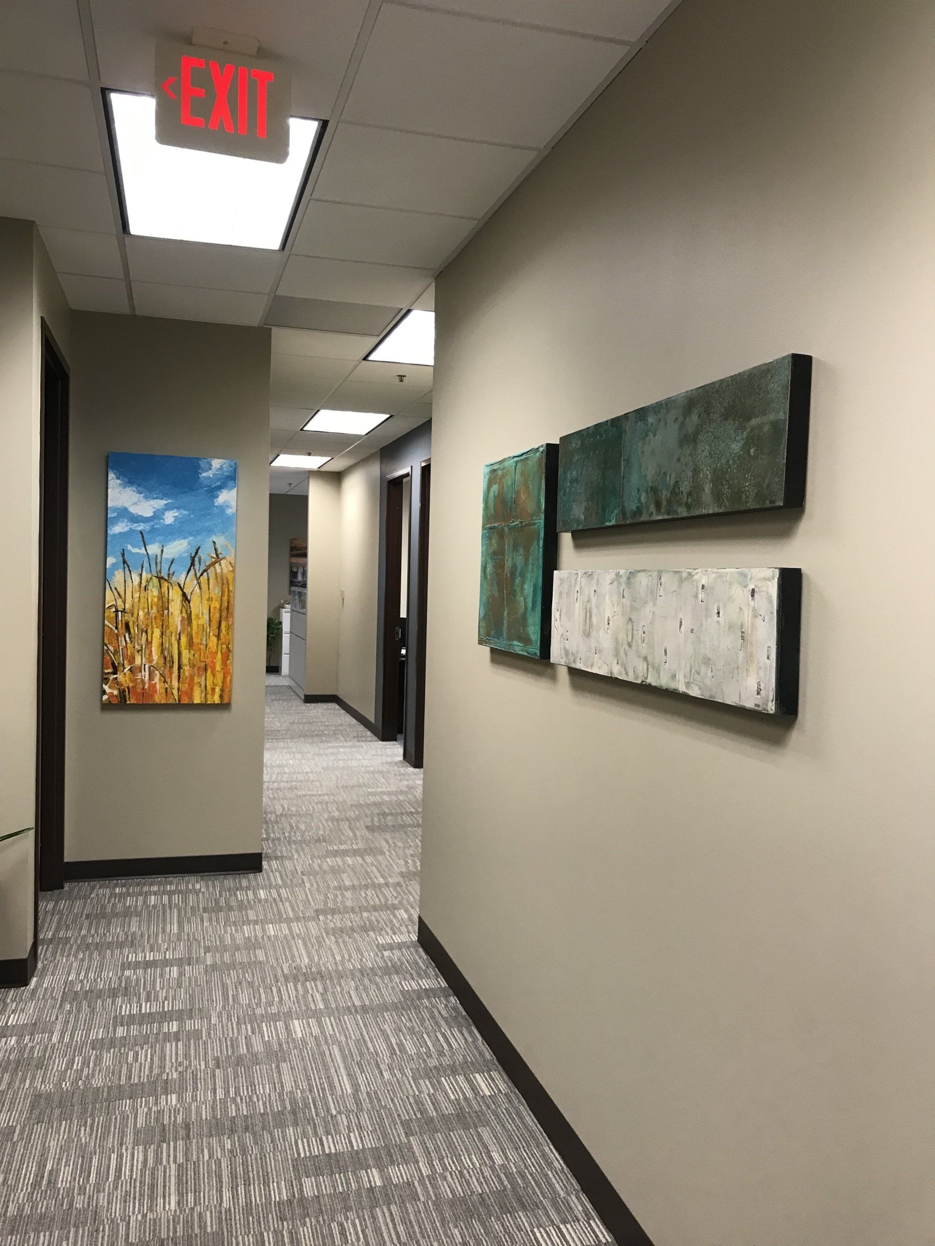 A hallway with paintings on the wall and an exit sign.