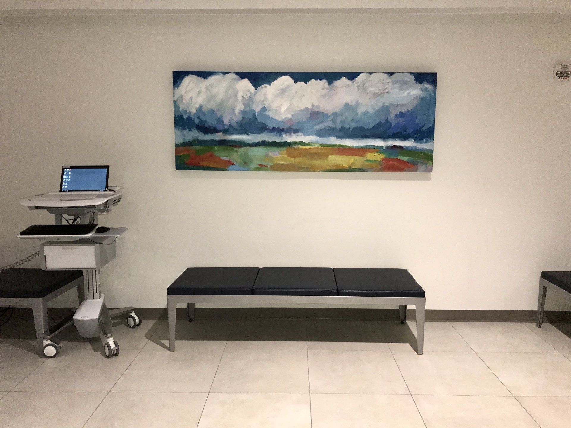 A painting hangs on a wall above a bench in a waiting room