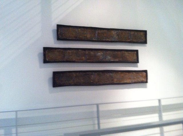 Three pieces of art are hanging on a white wall