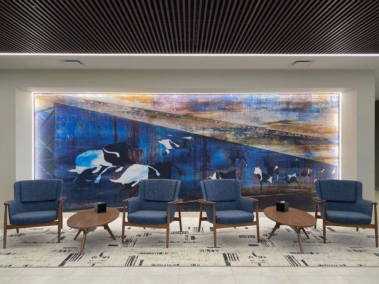 A waiting room with chairs and tables and a large painting on the wall.