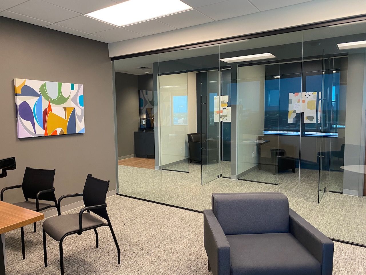 A waiting room with chairs , a chair , a table and a painting on the wall.