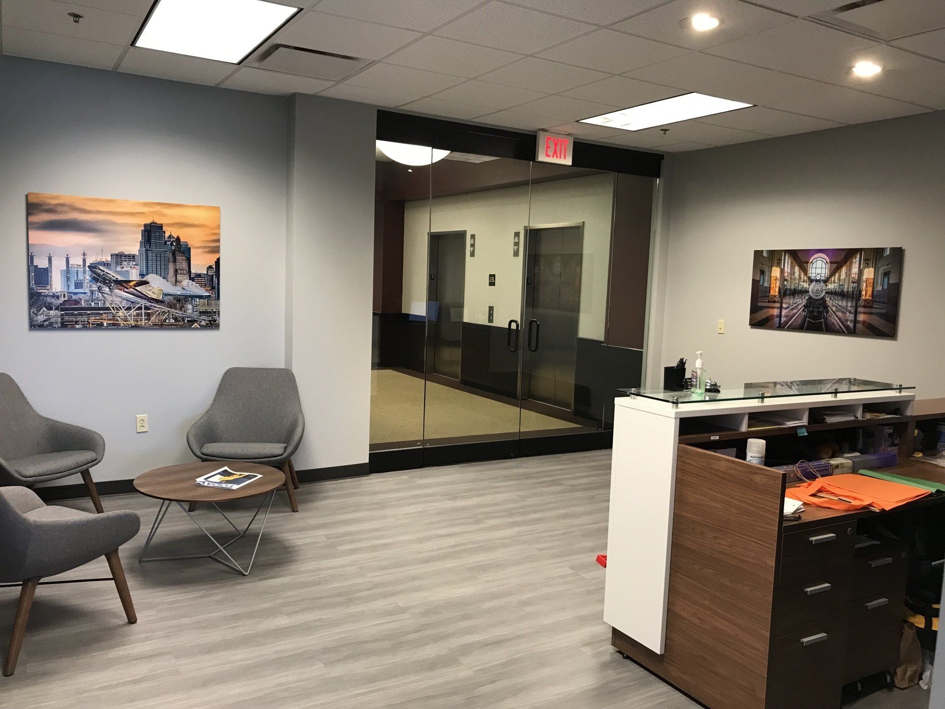 A waiting room with chairs , a table , and a painting on the wall.