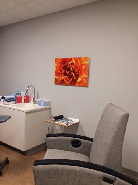 A painting of a flower hangs on a wall above a chair