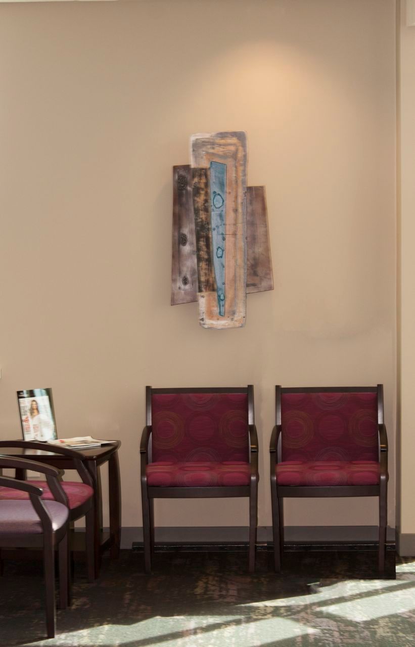 A waiting room with red chairs and a painting on the wall.
