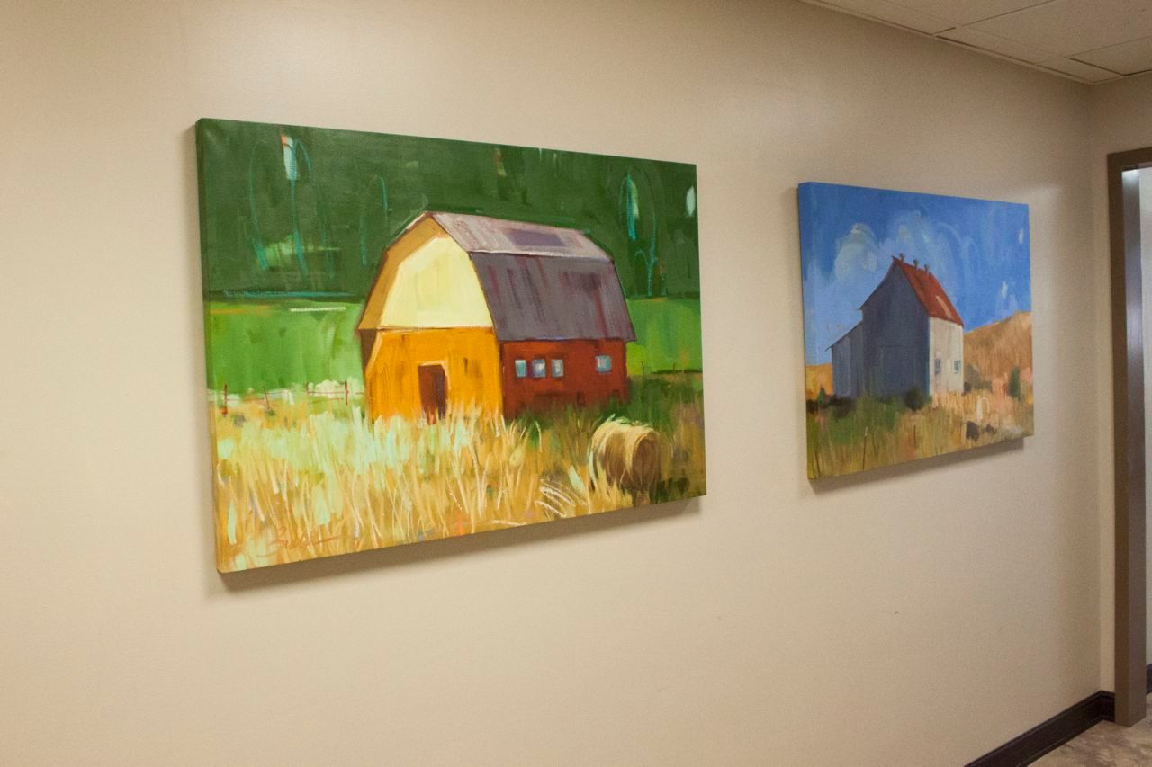 Two paintings of barns are hanging on a wall in a hallway.