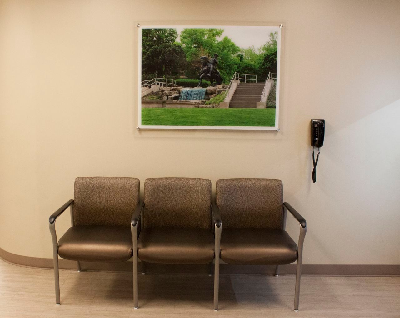 Three chairs in a waiting room with a picture on the wall above them