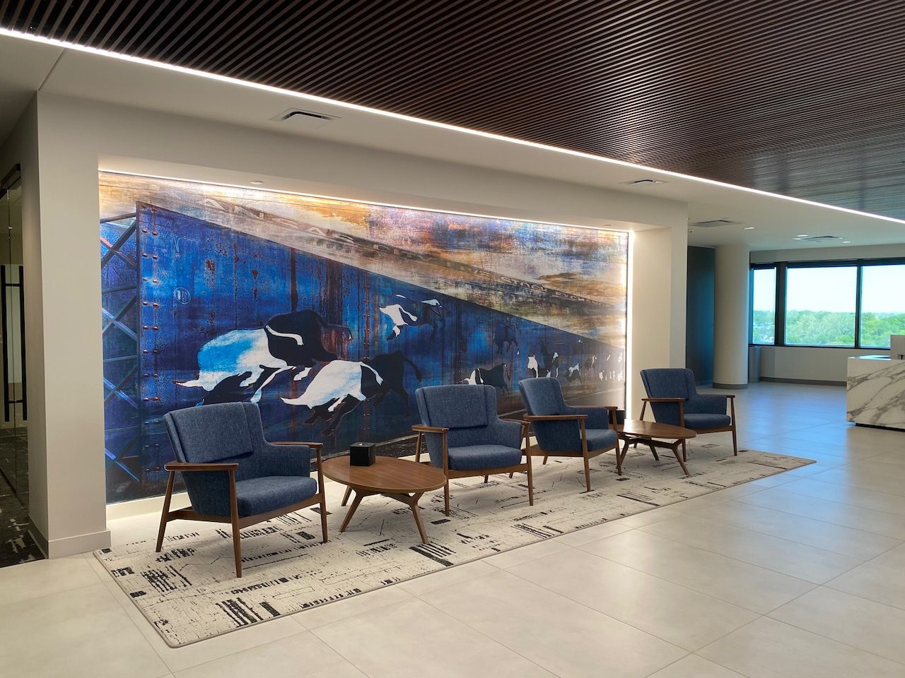 A waiting room with chairs , tables and a large painting on the wall.